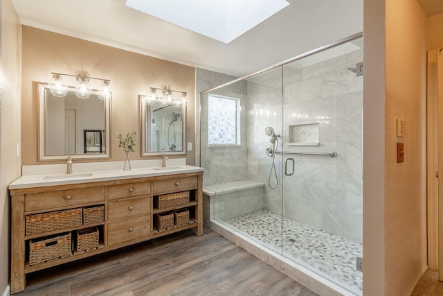 bathroom featuring a skylight, a shower stall, wood finished floors, and a sink