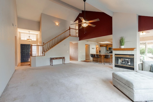 unfurnished living room with beam ceiling, ceiling fan, stairs, a tile fireplace, and light carpet