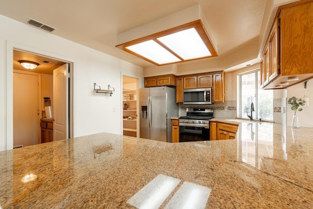 kitchen with brown cabinets, light stone counters, visible vents, and stainless steel appliances