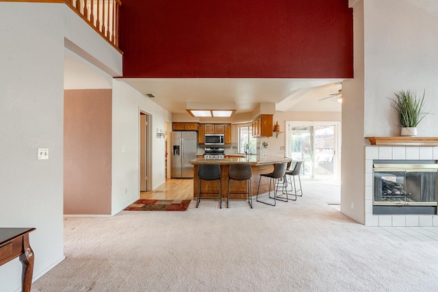 kitchen with stainless steel appliances, a peninsula, a fireplace, brown cabinetry, and light colored carpet