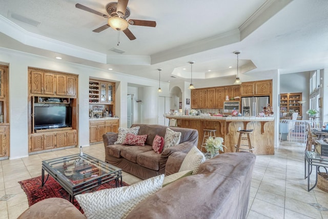 living area featuring light tile patterned floors, a raised ceiling, arched walkways, and ornamental molding