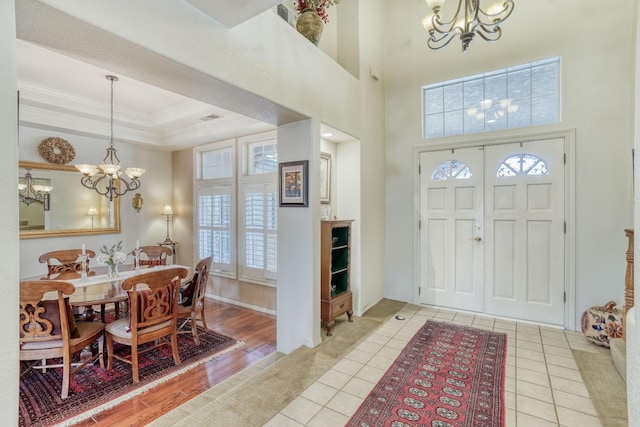 foyer with a chandelier, light wood finished floors, a raised ceiling, and ornamental molding