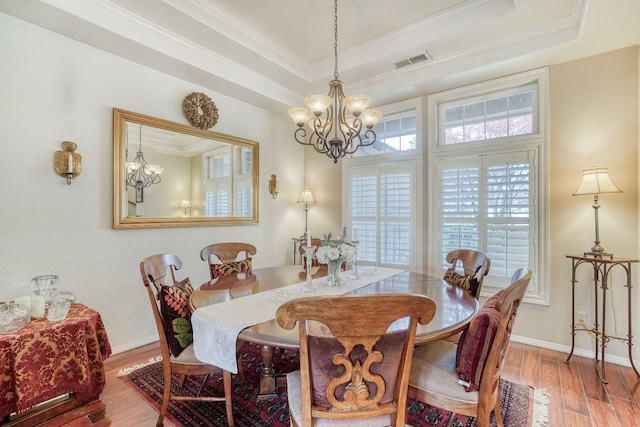 dining room featuring visible vents, a tray ceiling, wood finished floors, crown molding, and a chandelier