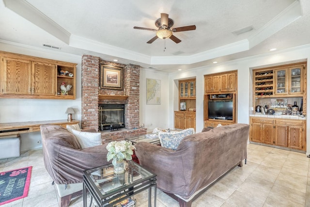 living area with a raised ceiling, crown molding, a fireplace, and visible vents