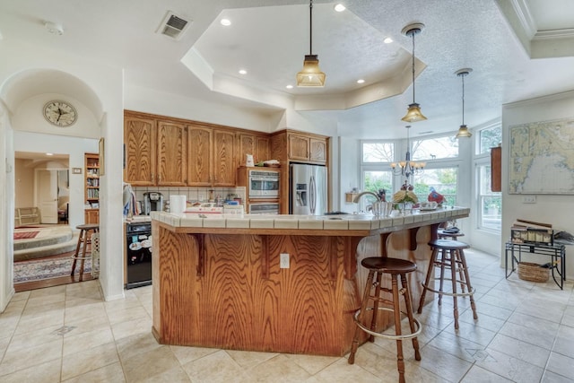 851 E Country View Cir, Fresno, CA 93730 - kitchen featuring stainless steel appliances, tile countertops, ornamental molding, brown cabinetry, and a tray ceiling