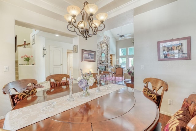 dining space with baseboards, a large fireplace, crown molding, and ceiling fan with notable chandelier