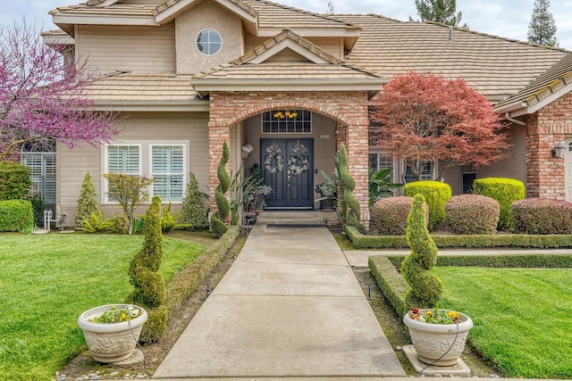 entrance to property with a tile roof, a lawn, and brick siding