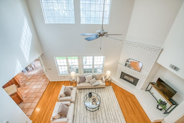 living area featuring a brick fireplace, a towering ceiling, and wood finished floors