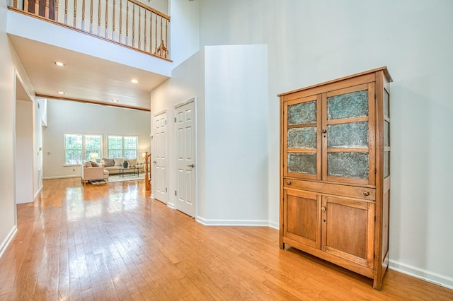 corridor with recessed lighting, baseboards, light wood-type flooring, and a towering ceiling