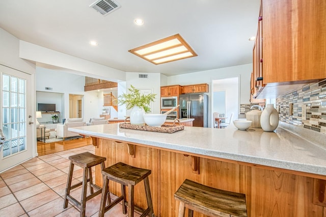 kitchen with brown cabinetry, visible vents, a peninsula, appliances with stainless steel finishes, and tasteful backsplash