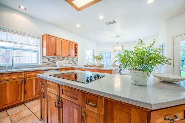 kitchen featuring decorative backsplash, black electric cooktop, brown cabinetry, and a healthy amount of sunlight