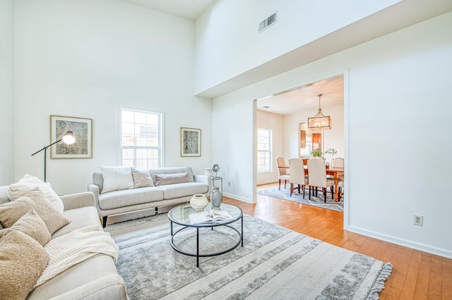 living room with visible vents, baseboards, a high ceiling, and light wood-style flooring