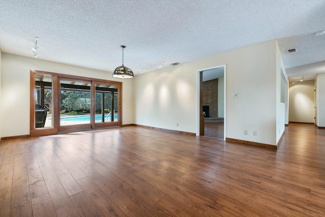 spare room with visible vents, a brick fireplace, a textured ceiling, and wood finished floors