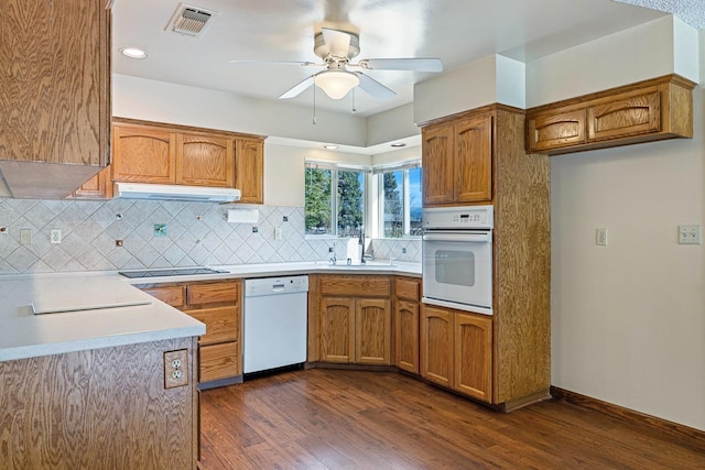 kitchen with white appliances, visible vents, a sink, under cabinet range hood, and brown cabinets