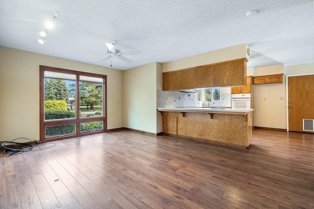 kitchen with oven, backsplash, a peninsula, brown cabinetry, and dark wood-style flooring