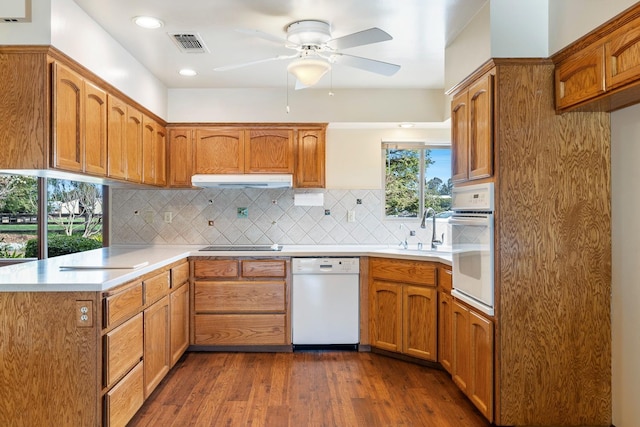 kitchen featuring visible vents, under cabinet range hood, decorative backsplash, white appliances, and a sink