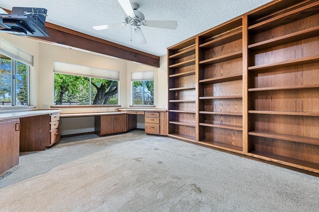 unfurnished office featuring a ceiling fan, light colored carpet, built in desk, and a textured ceiling