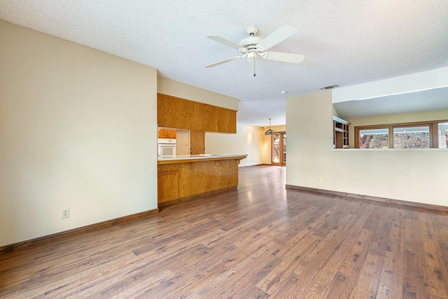 unfurnished living room featuring a textured ceiling, dark wood-type flooring, baseboards, and ceiling fan