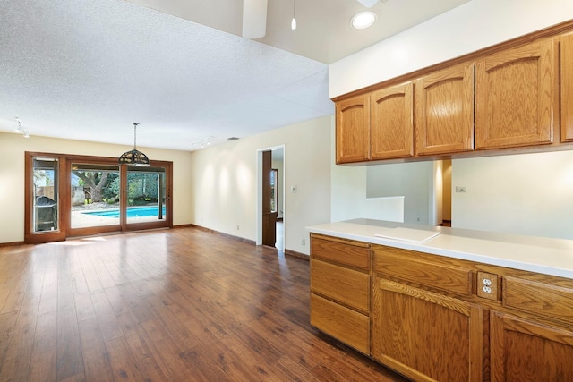 kitchen featuring brown cabinetry, dark wood-style floors, baseboards, light countertops, and open floor plan