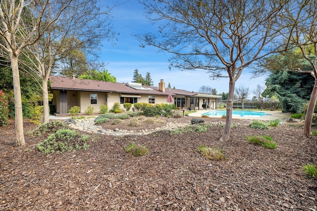 rear view of house featuring stucco siding, an outdoor pool, and a chimney