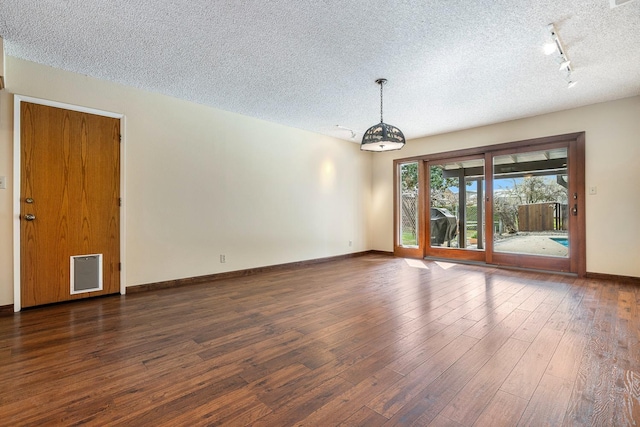 empty room featuring dark wood finished floors, rail lighting, a textured ceiling, and baseboards