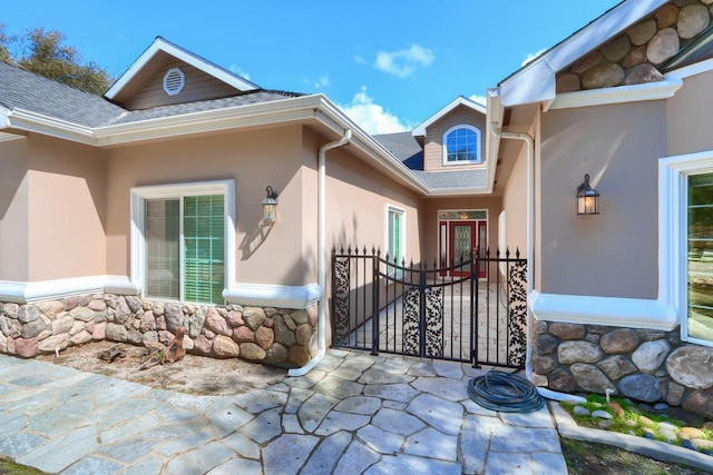 entrance to property featuring stone siding, roof with shingles, and stucco siding