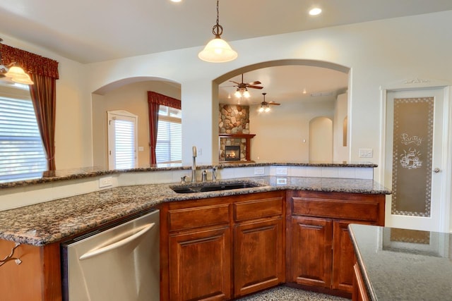 kitchen with ceiling fan, dishwasher, dark stone countertops, a fireplace, and a sink