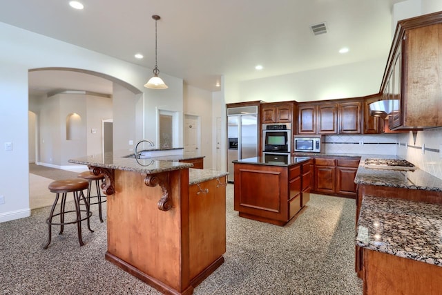 kitchen featuring visible vents, a kitchen island with sink, backsplash, stainless steel appliances, and arched walkways