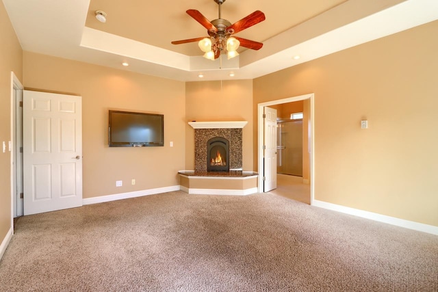 unfurnished living room featuring a warm lit fireplace, a raised ceiling, baseboards, and carpet floors