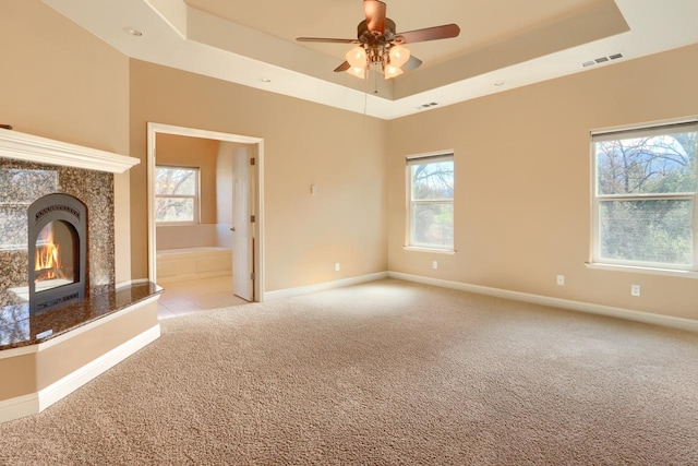 unfurnished living room featuring a high end fireplace, visible vents, light colored carpet, and a tray ceiling