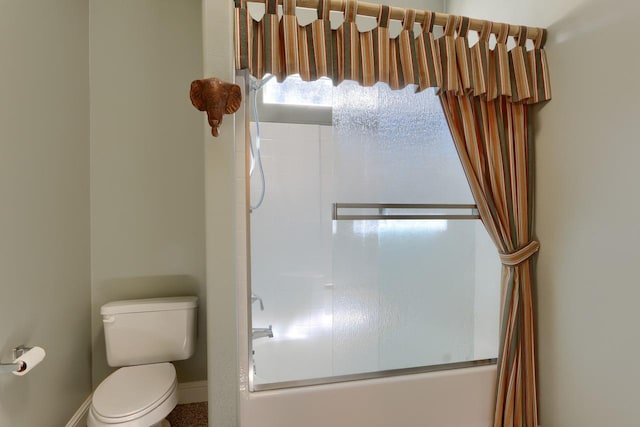 bathroom with toilet, baseboards, and shower / bath combination with glass door