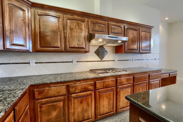 kitchen with under cabinet range hood, decorative backsplash, stainless steel gas cooktop, and dark stone counters