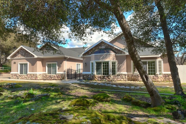 exterior space featuring a gate, fence, stone siding, and stucco siding