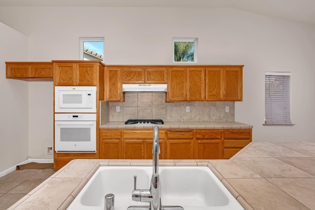 kitchen with under cabinet range hood, decorative backsplash, white appliances, and a sink