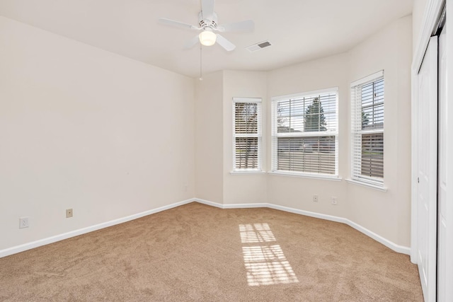 empty room with light carpet, visible vents, ceiling fan, and baseboards