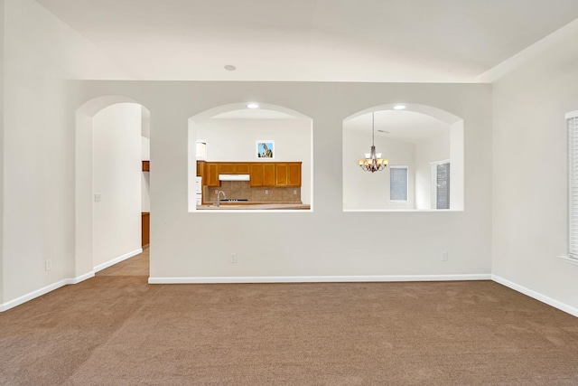 carpeted spare room with a notable chandelier, baseboards, and a sink