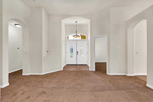 entryway with tile patterned floors, baseboards, carpet, a towering ceiling, and arched walkways