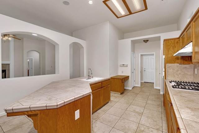 kitchen with under cabinet range hood, tile countertops, tasteful backsplash, and a sink