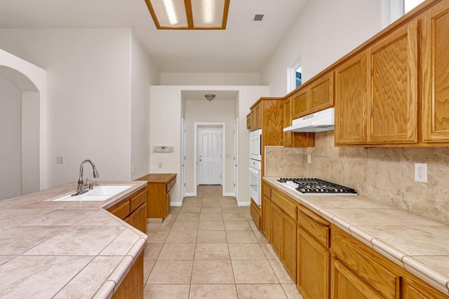 kitchen with under cabinet range hood, a sink, tasteful backsplash, white appliances, and tile counters