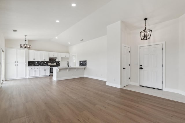 819 Hill Ave, Fowler, CA 93625 - unfurnished living room with a chandelier, light wood-style floors, baseboards, high vaulted ceiling, and a sink