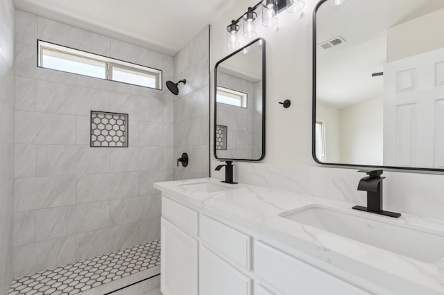 bathroom featuring a sink, visible vents, tiled shower, and double vanity