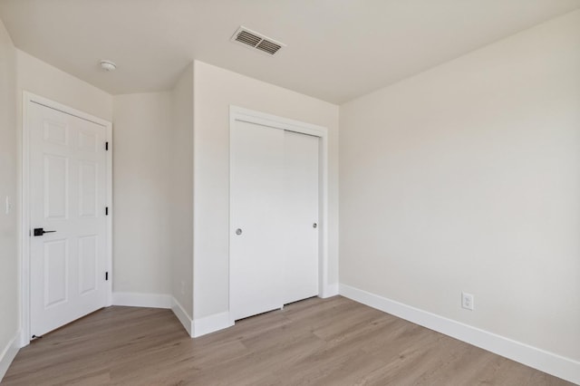 unfurnished bedroom with light wood-type flooring, baseboards, visible vents, and a closet