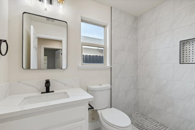 bathroom with a tile shower, visible vents, toilet, and vanity