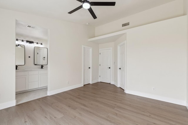 unfurnished bedroom with light wood finished floors, visible vents, ensuite bathroom, and baseboards