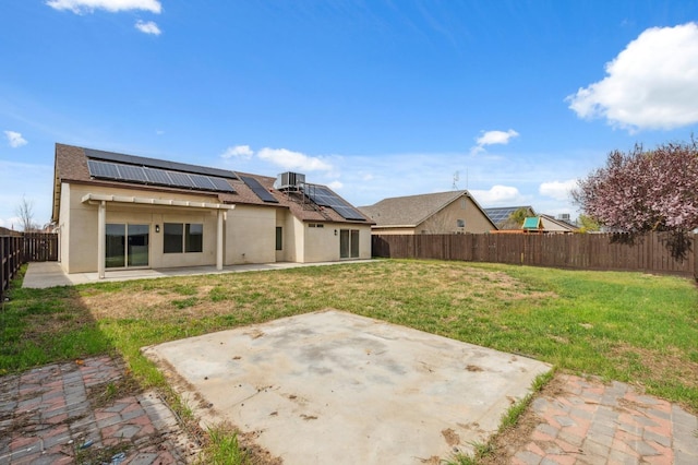 rear view of property featuring stucco siding, a lawn, a patio, a fenced backyard, and solar panels