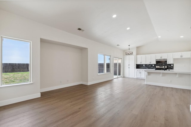 unfurnished living room featuring light wood-type flooring, visible vents, recessed lighting, baseboards, and vaulted ceiling