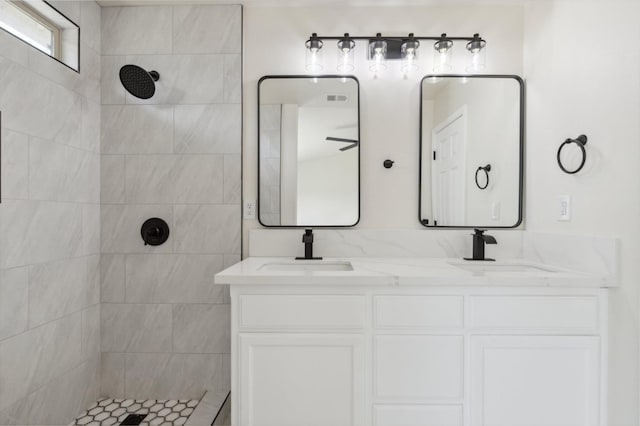 full bath featuring a sink, tiled shower, and double vanity