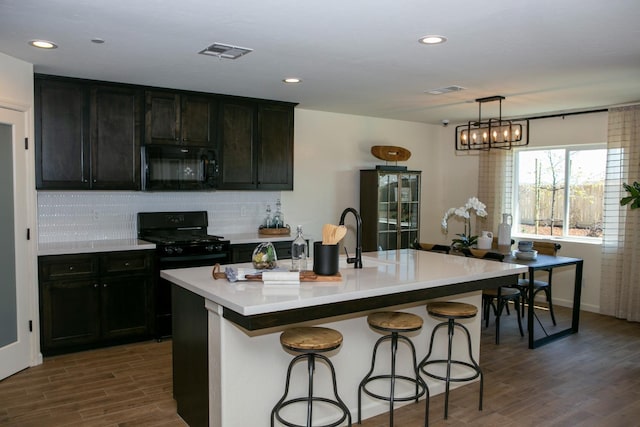 kitchen with a breakfast bar area, visible vents, dark wood finished floors, black appliances, and tasteful backsplash