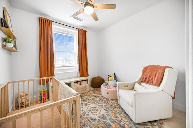 bedroom featuring visible vents, a nursery area, light colored carpet, and a ceiling fan