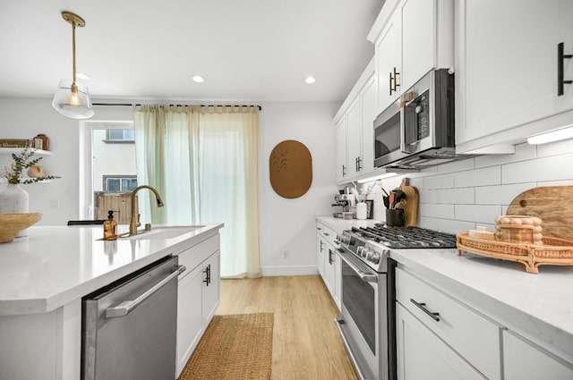 kitchen featuring light wood finished floors, backsplash, light countertops, stainless steel appliances, and a sink